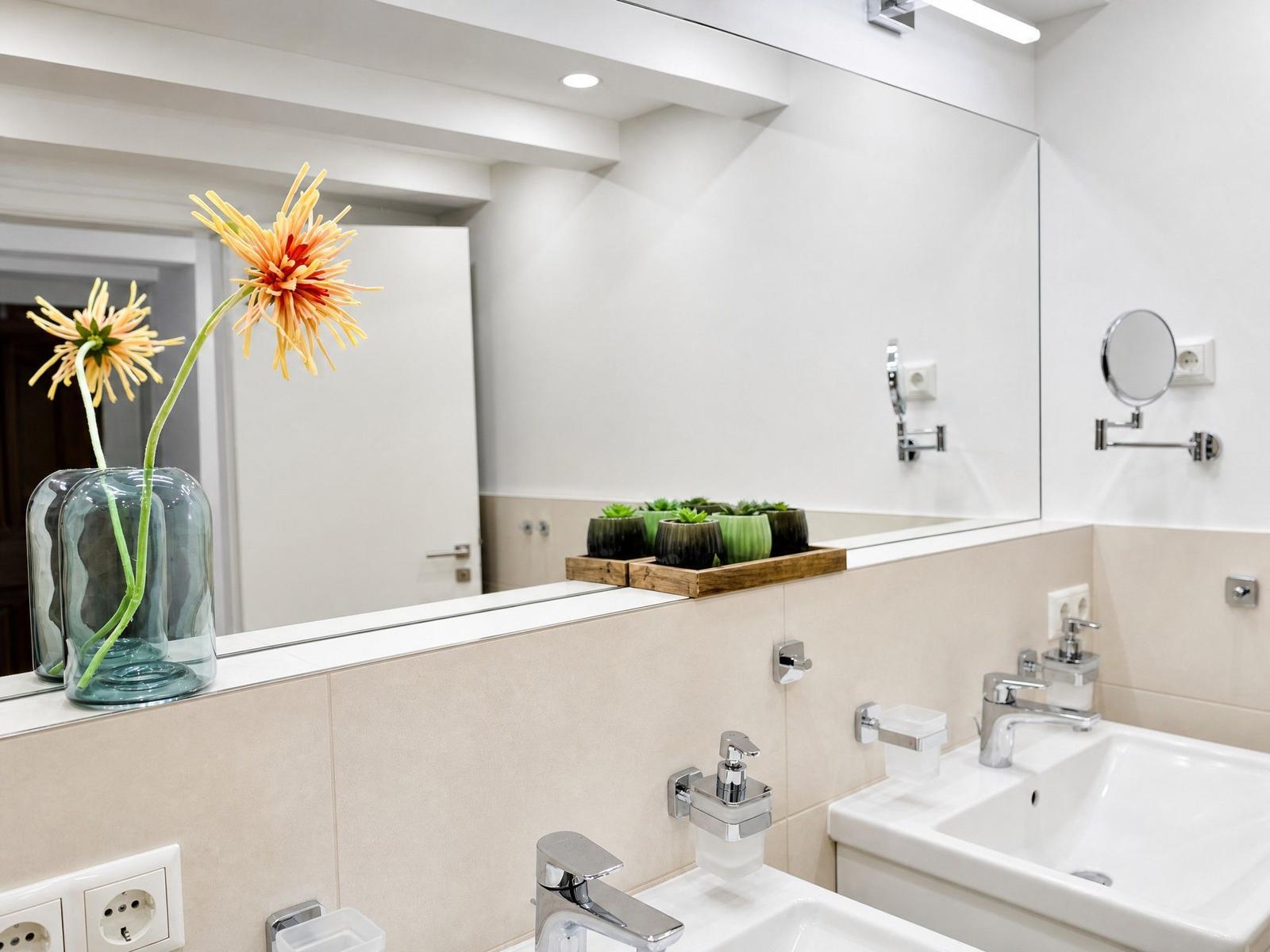 Bad mit Waschbecken, Spiegel und Blumen im Glasbehälter.