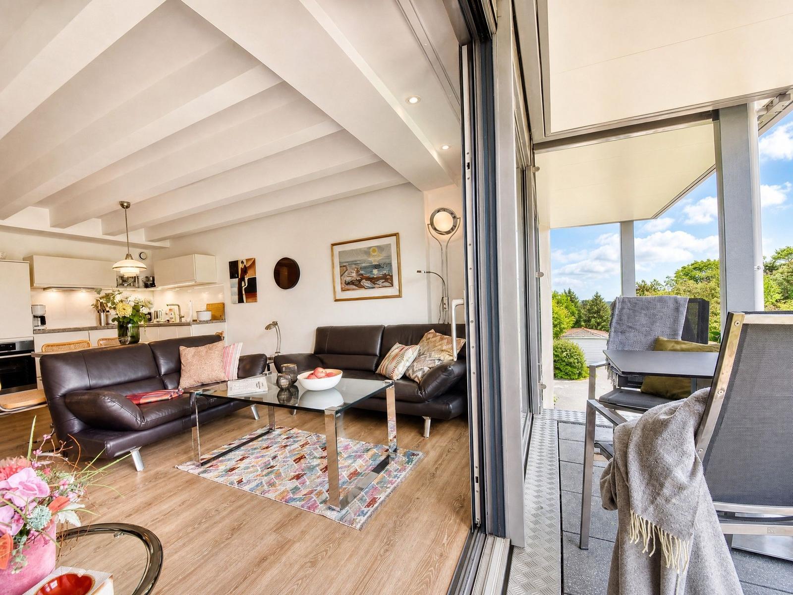 Wohnzimmer mit Sofa, Couchtisch und Terrasse mit Blick auf Grünflächen.