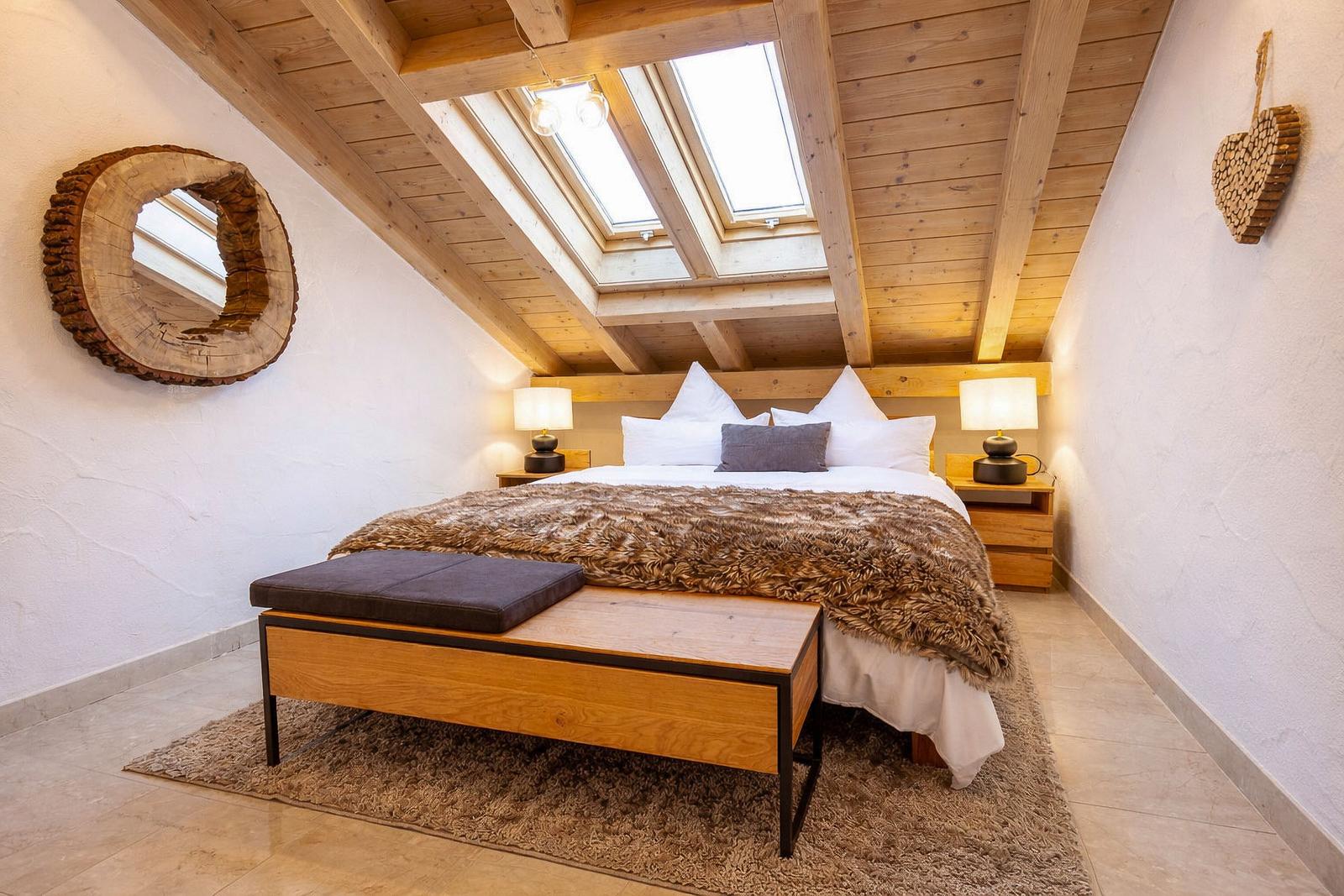 Schlafzimmer mit Dachboden, Holzdecke, Fenster und Bett mit Felldecke.