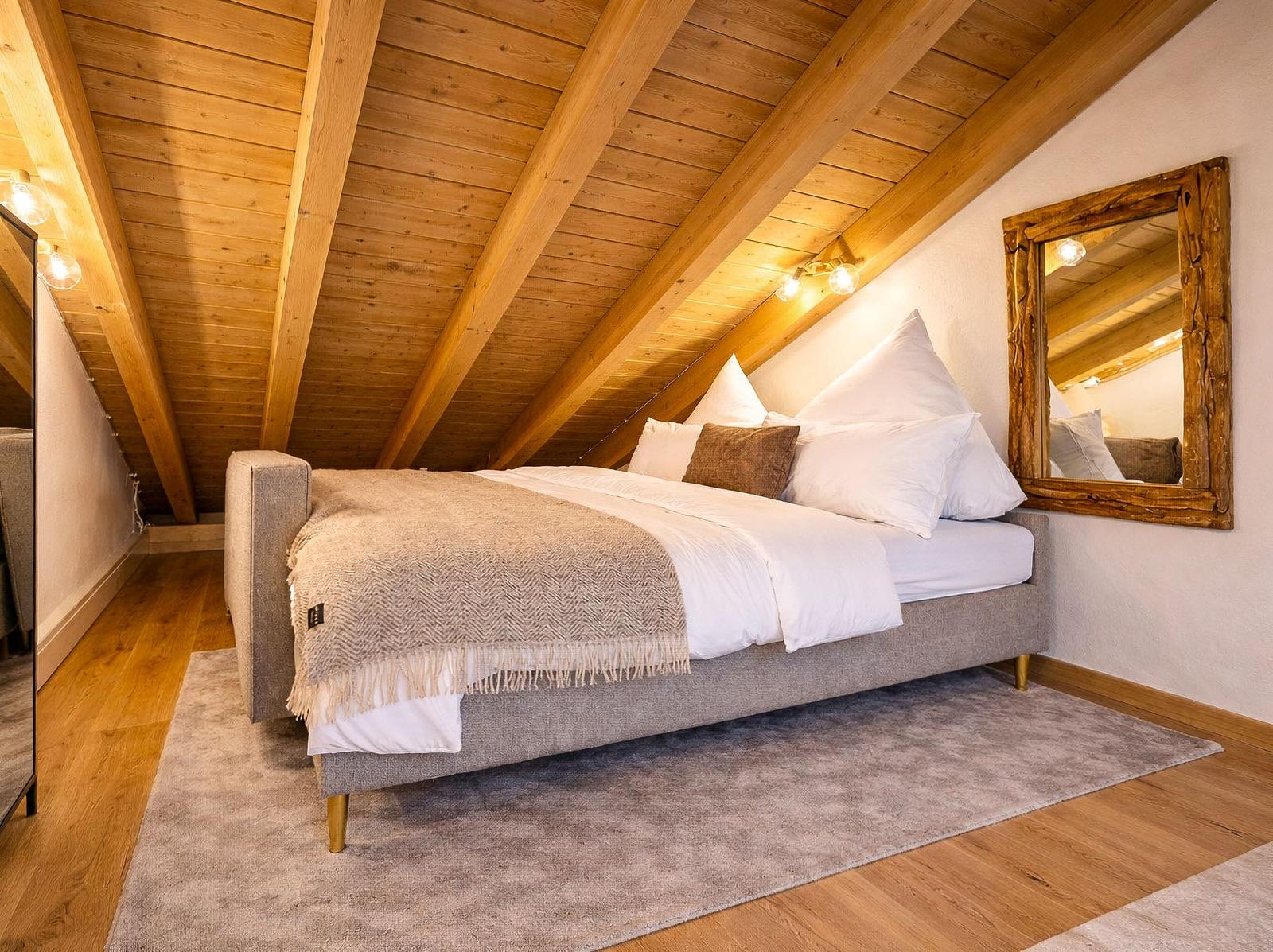Schlafzimmer mit Holzdecke, Bett, Spiegel und Teppich.