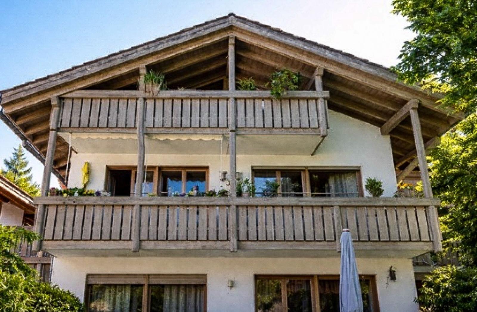 Haus mit zwei Balkonen, Holzverkleidung und Pflanzen. Umgeben von Bäumen.