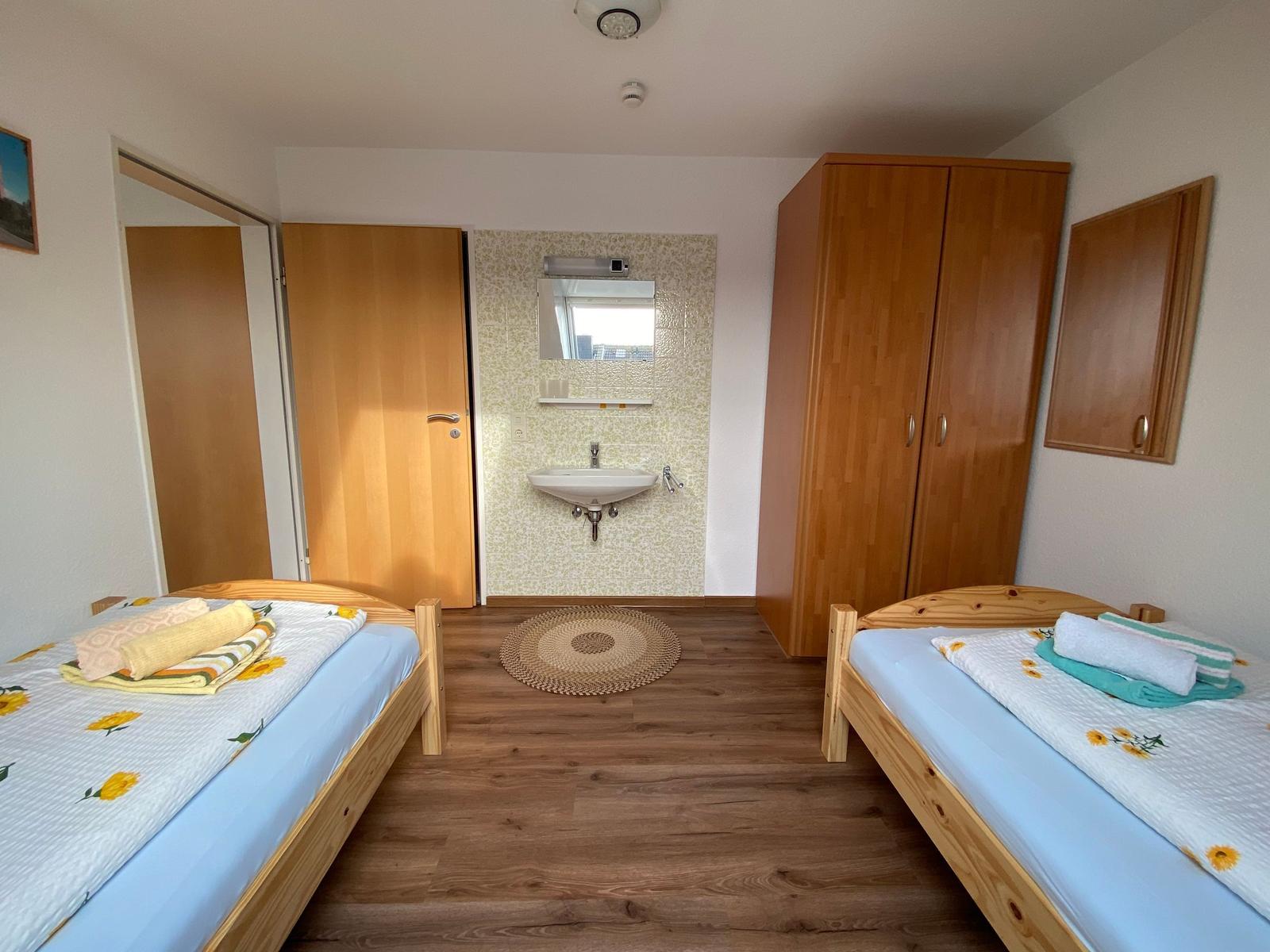 Zwei Einzelbetten, Holzmöbel und Waschbecken im Badebereich.