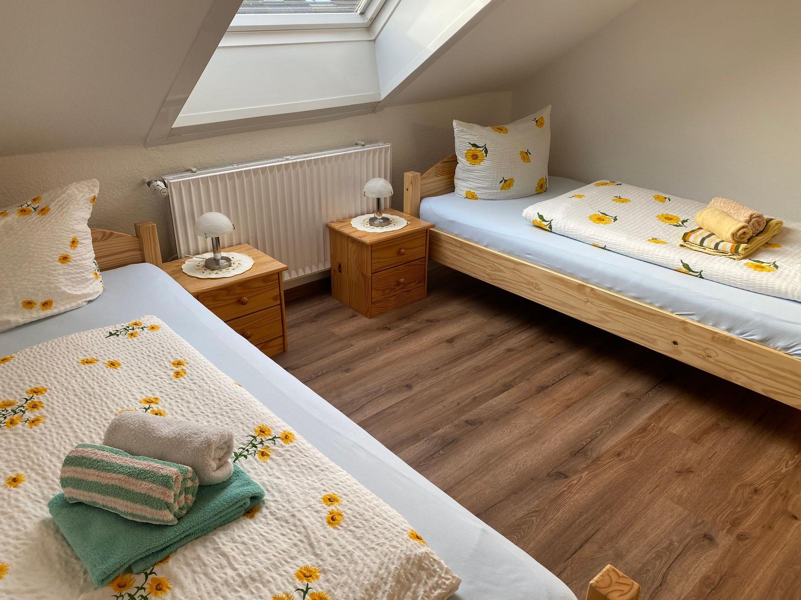 Zwei Betten mit Sonnenblumenbezug, Holzfußböden und Dachschrägen mit Fenster.