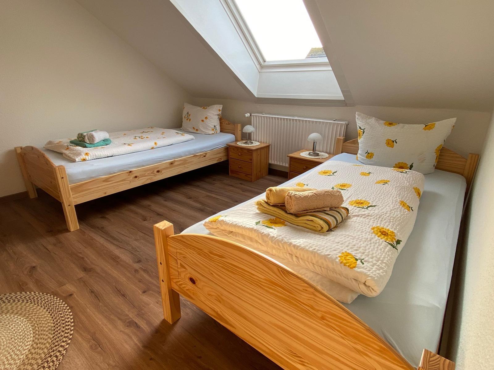 Zimmer mit zwei Betten, Dachschräge und Dachfenster. Holzboden und Nachttische.