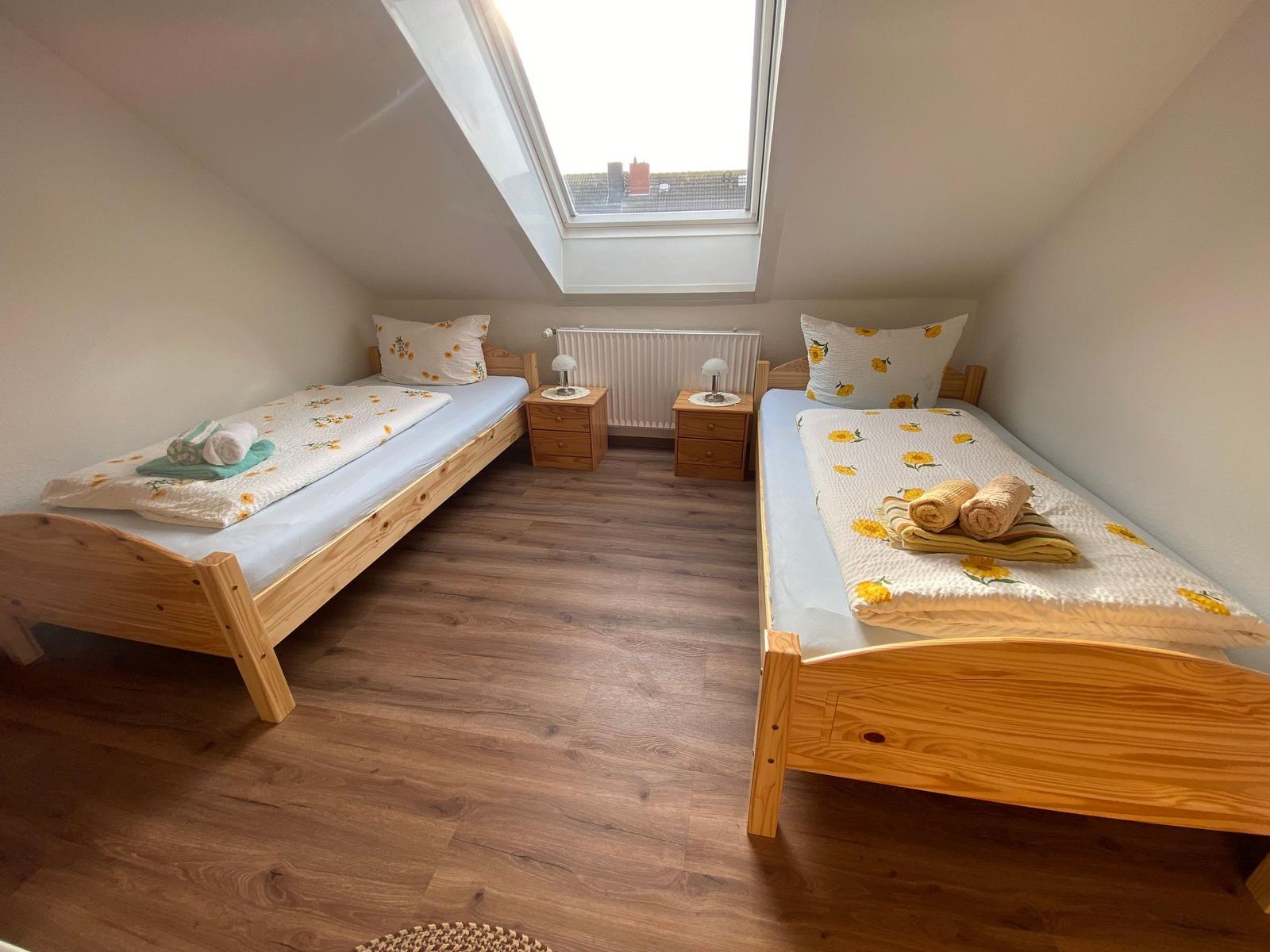 Zwei Einzelbetten mit Sonnenblumenbezug, Holzfußboden und Dachfenster.