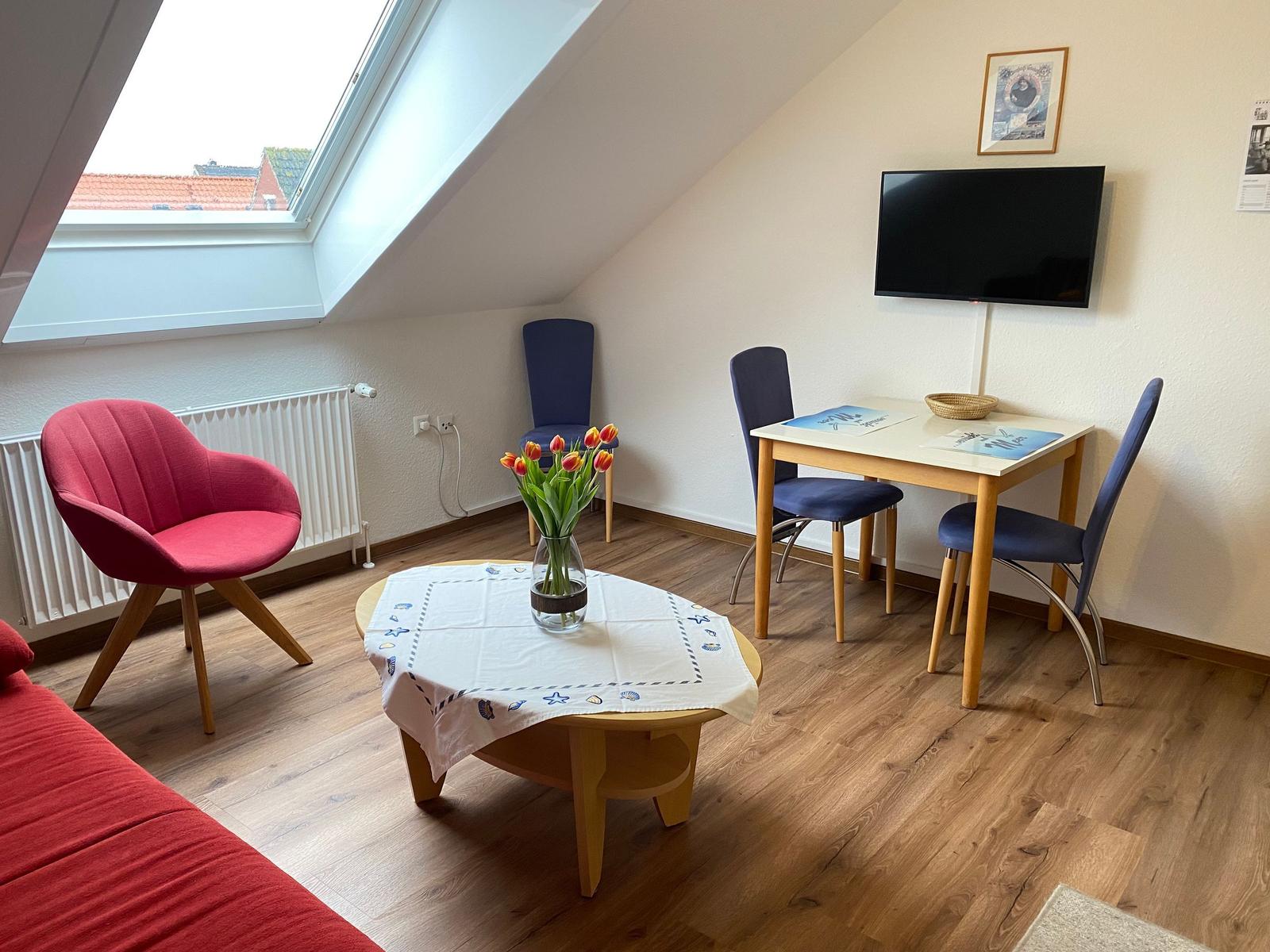 Wohnzimmer mit Dachfenster, Esstisch, TV und rotem Sessel.