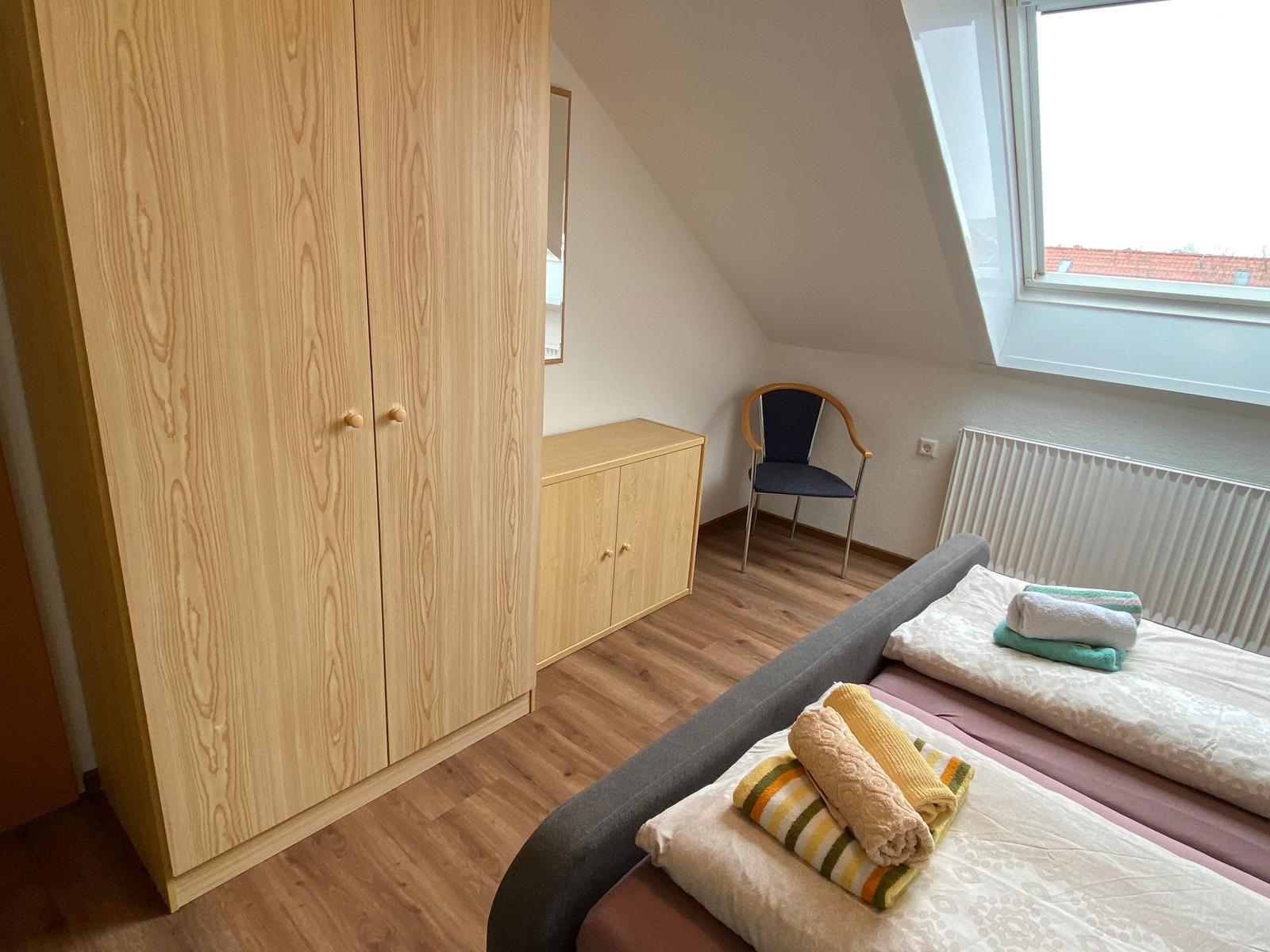 Schlafzimmer mit Dachschrägen, Bett, Kleiderschrank und Stuhl.