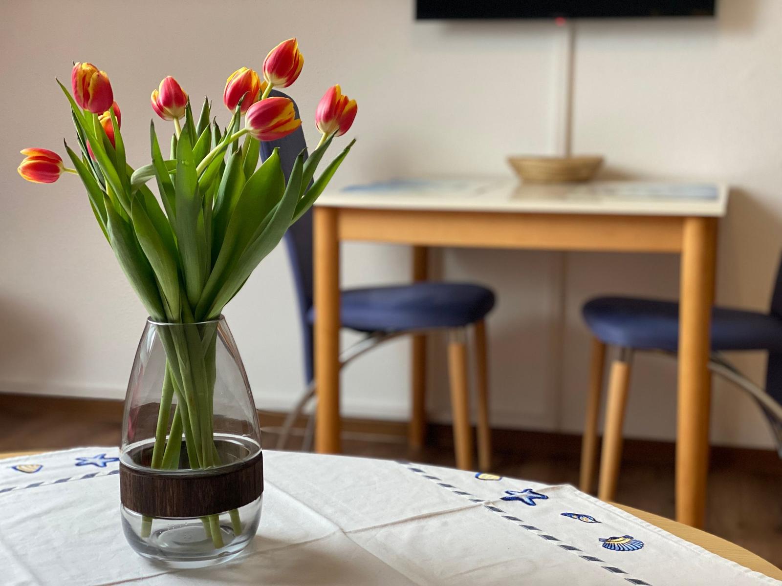 Auf dem Tisch steht eine Vase mit Tulpen. Im Hintergrund ist ein Esstisch mit Stühlen zu sehen.
