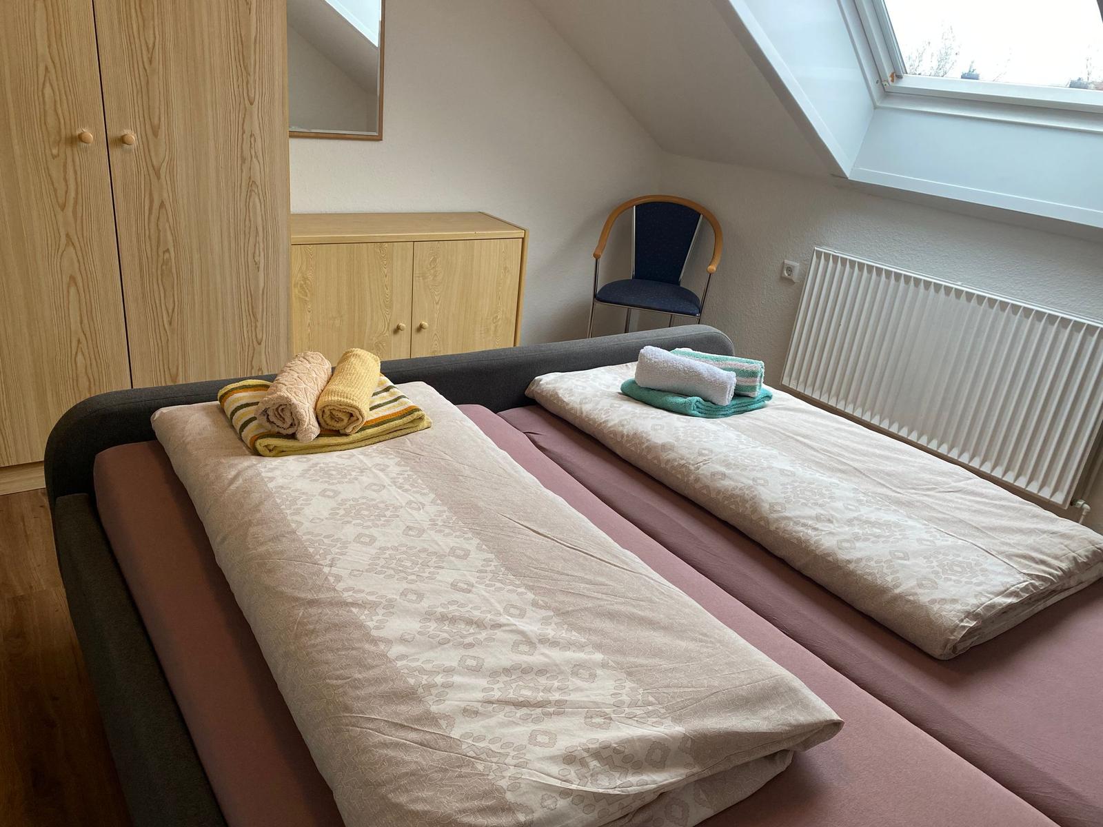 Zwei Betten mit Bettwäsche und Handtüchern. Holzschrank, Stuhl und Dachfenster.