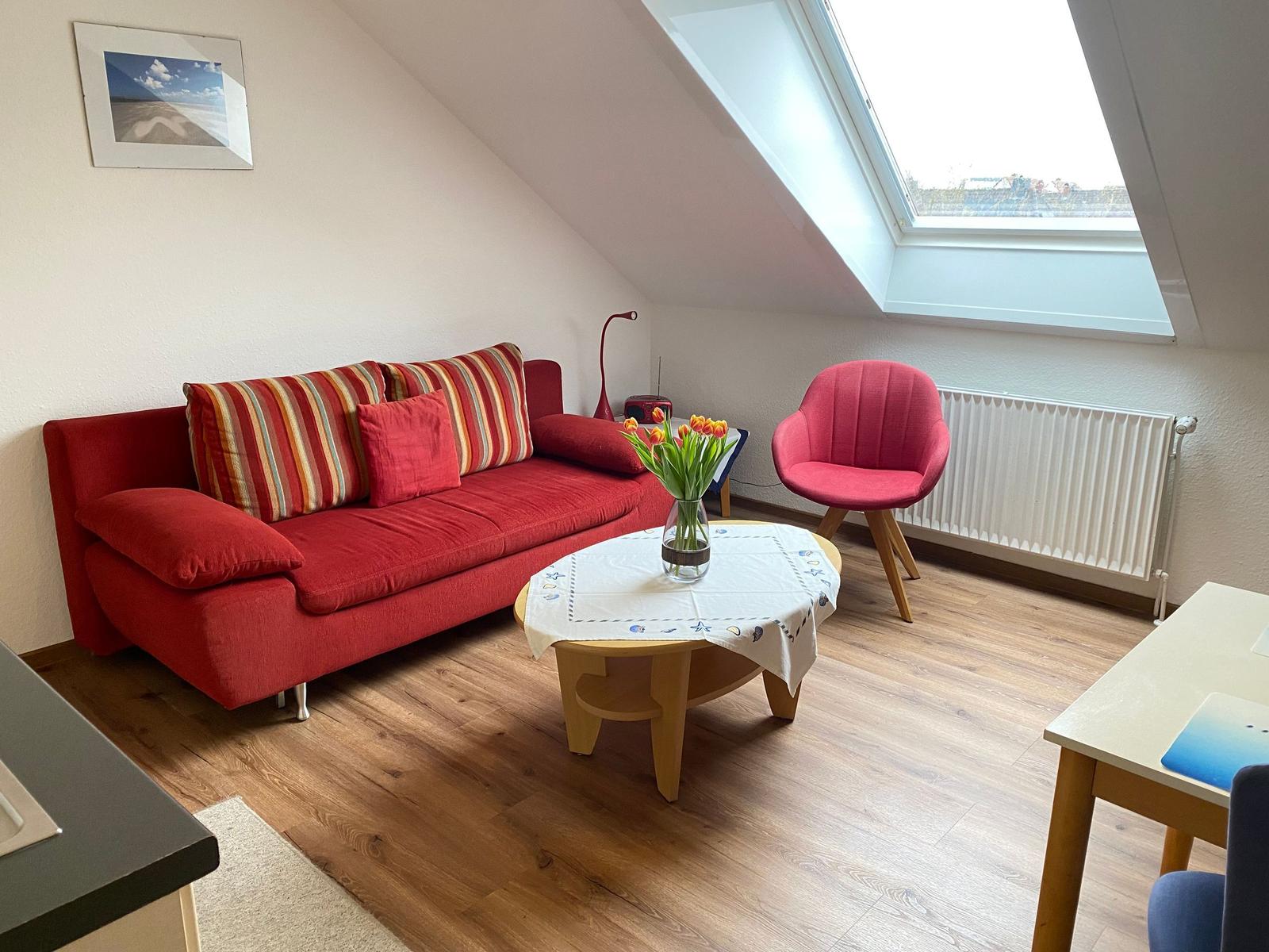 Wohnzimmer mit rotem Sofa, Stuhl und Tisch unter Dachfenster.