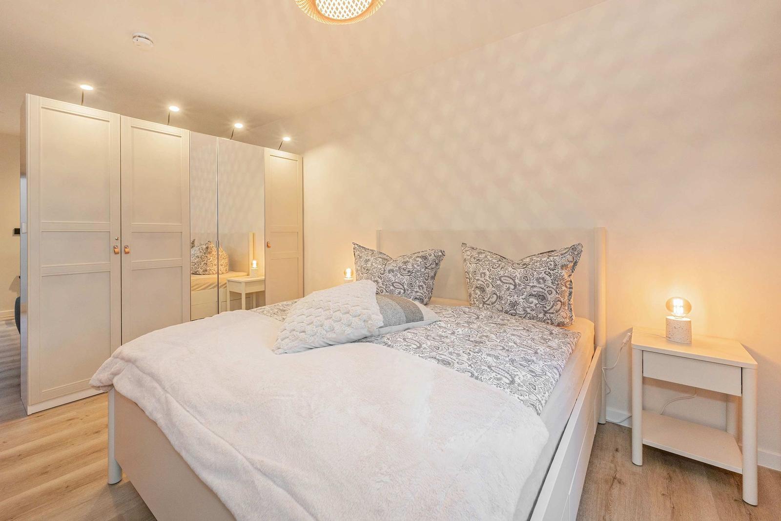 Bedroom with bed, nightstand, and wardrobe. Wall with pattern. Ceiling light and table lamp.