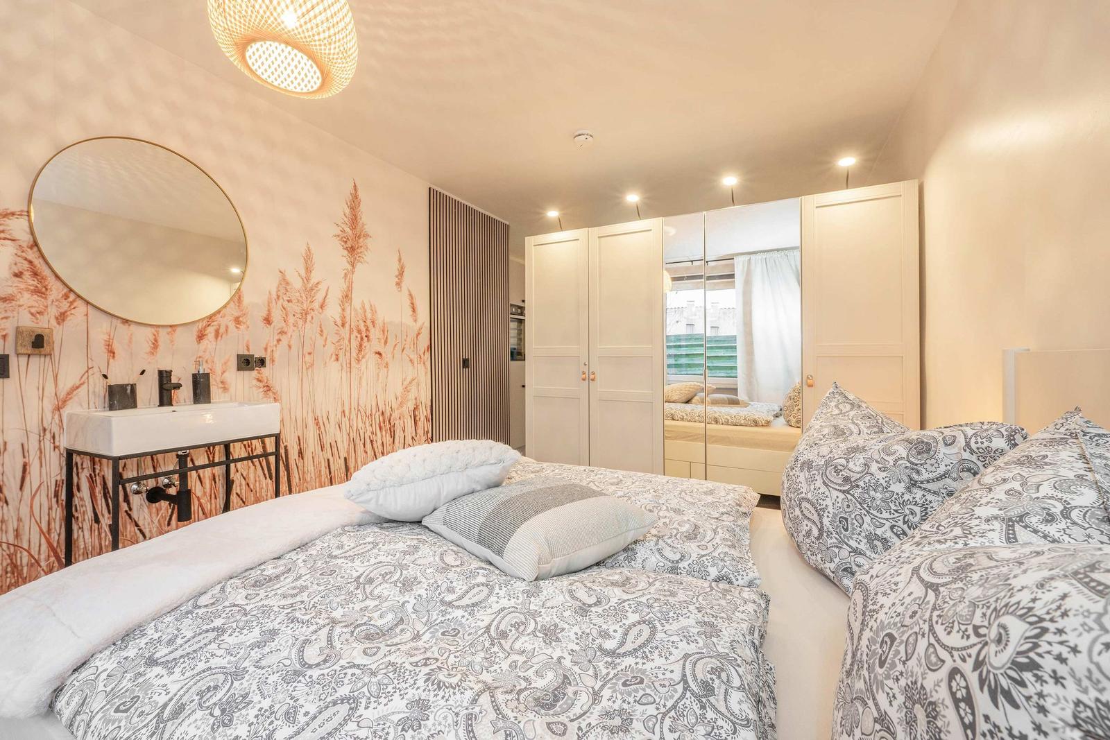 Bedroom with bed, wardrobe, and sink against wall with plant pattern.