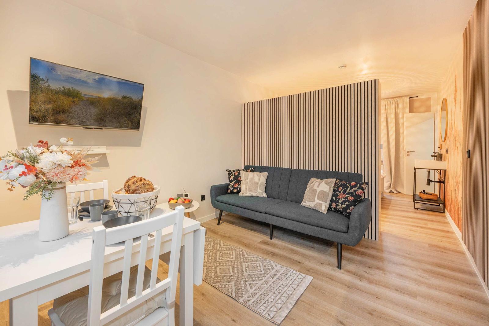 Living and dining area with sofa, table, and TV. Wooden floor and wall cladding.