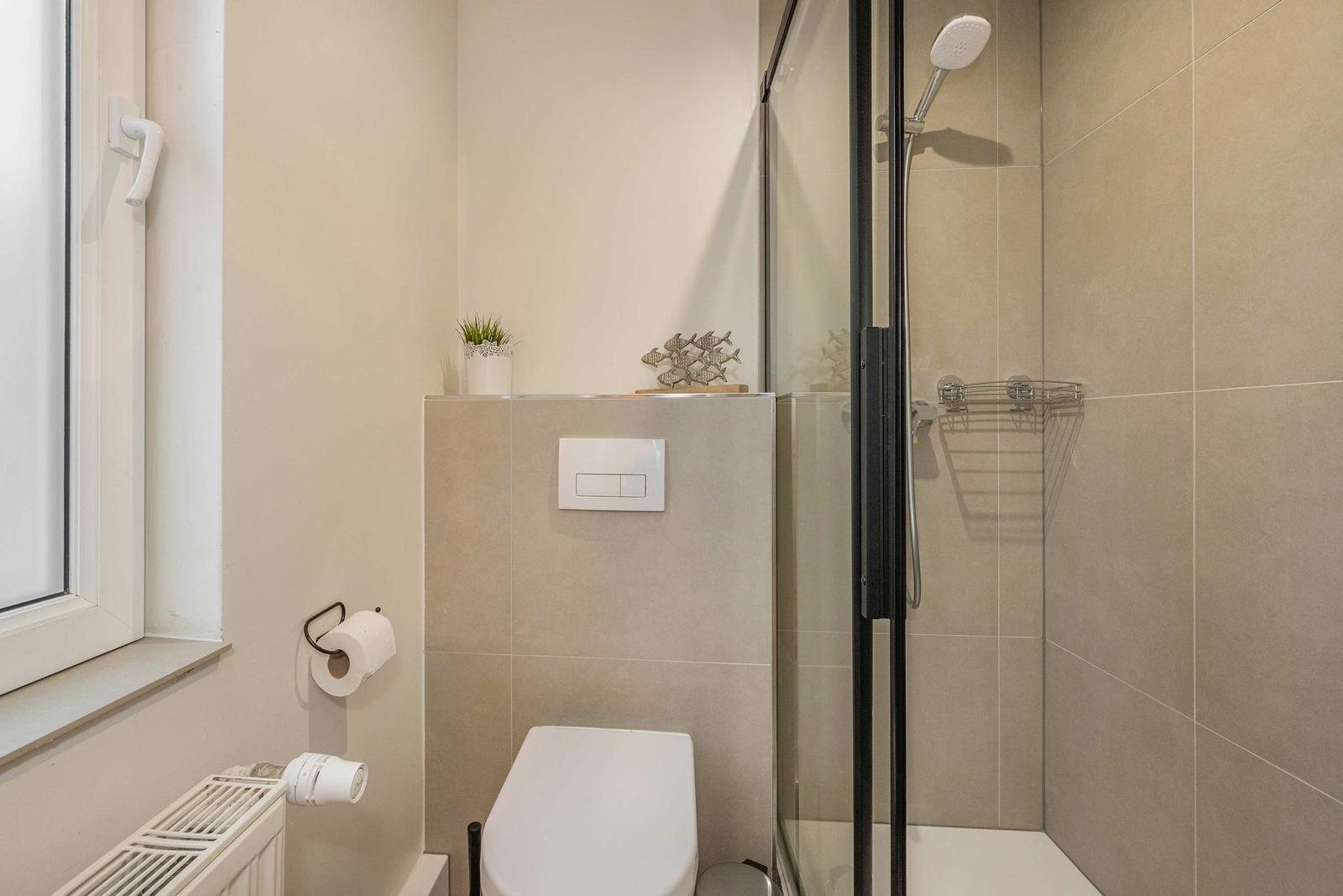 Bathroom with shower, toilet, and window. Shower base with glass wall and handheld shower.