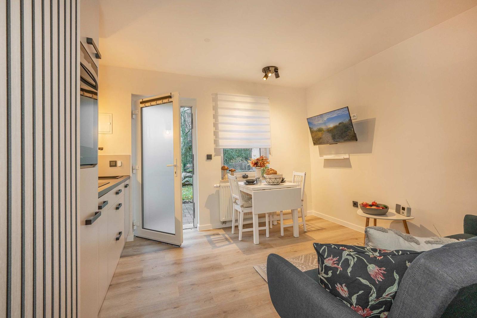 Living area with dining space, TV, and kitchen. Door leads to balcony.