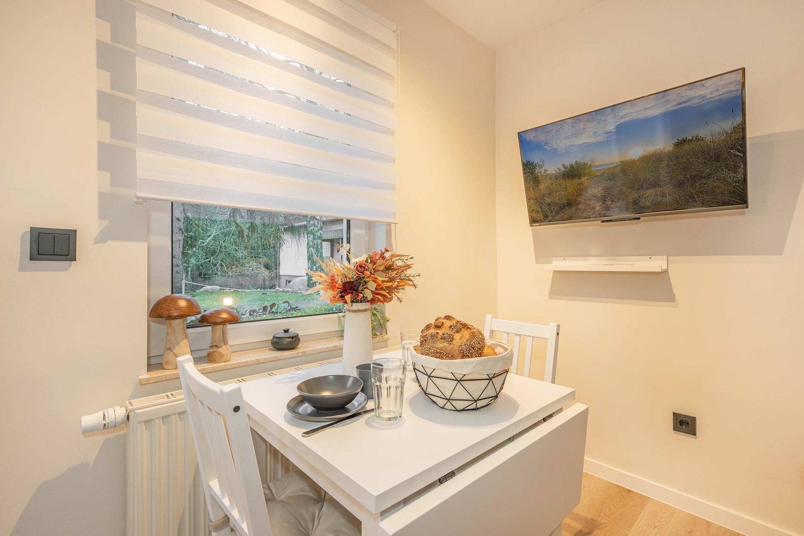 Dining room with table, chairs, and window view. Wall art and floral arrangement.
