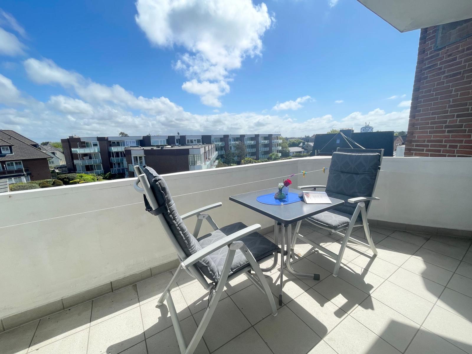Terrasse mit Tisch und zwei Stühlen, Blick auf Wohngebiet unter blauem Himmel.
