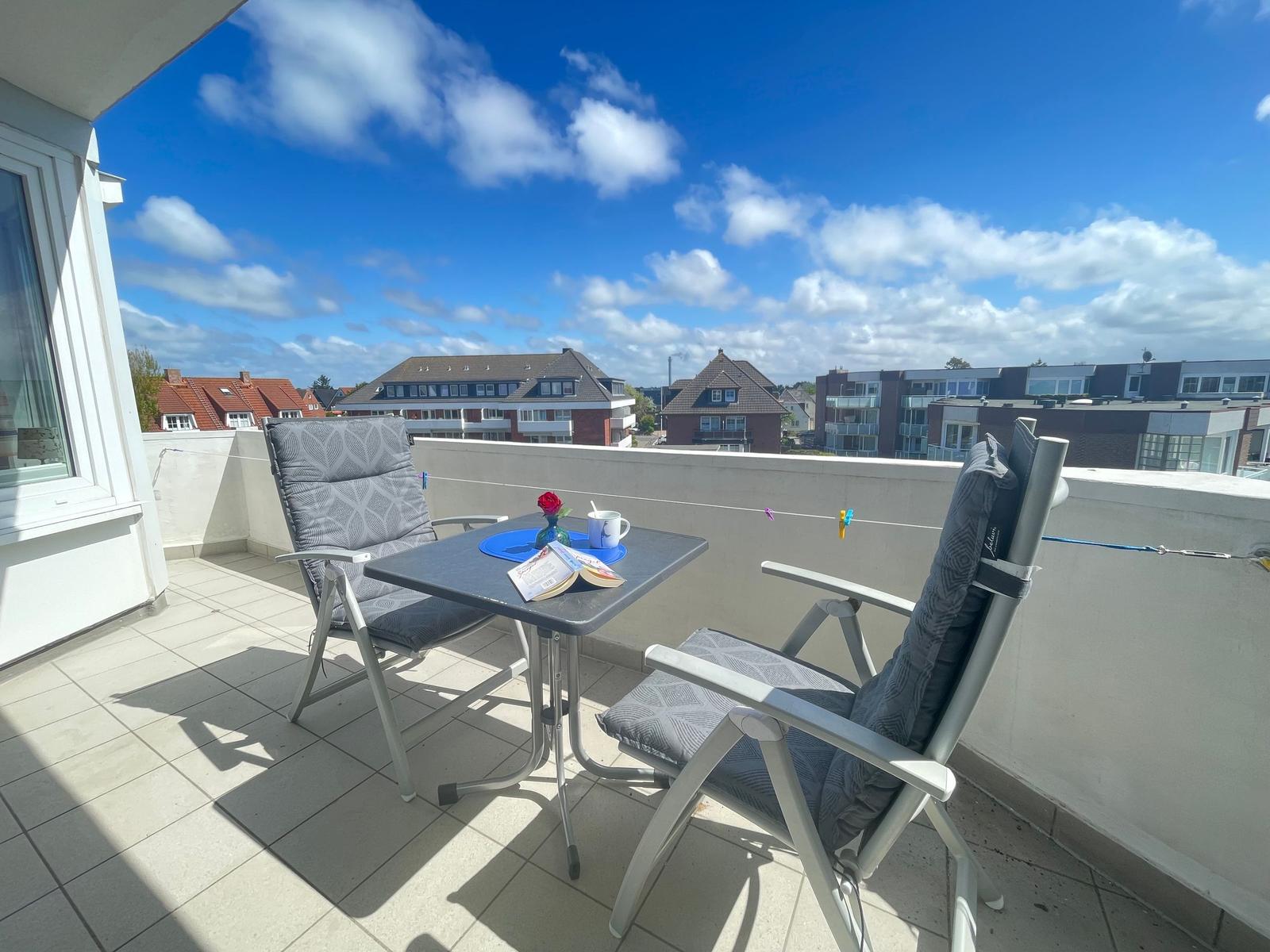 Terrasse mit Tisch und zwei Stühlen. Blick auf Wohngebiet unter blauem Himmel.