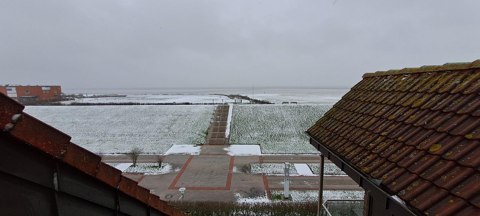 Schneebedeckte Landschaft mit Blick auf das Meer und roten Dächern.