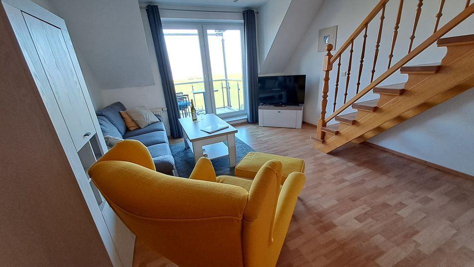 Wohnzimmer mit gelbem Sessel, Sofa, Fernseher und Balkonzugang.