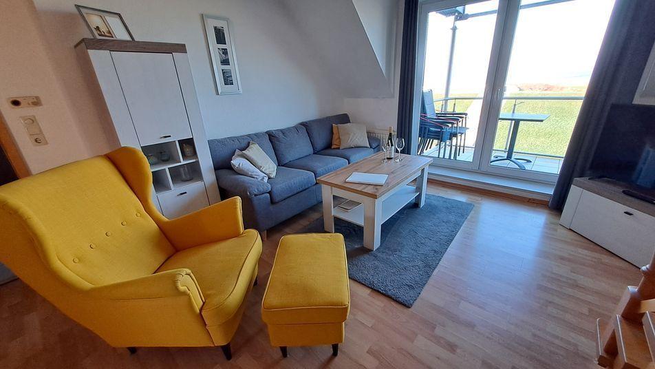 Wohnzimmer mit gelbem Sessel, grauem Sofa und Balkonansicht.
