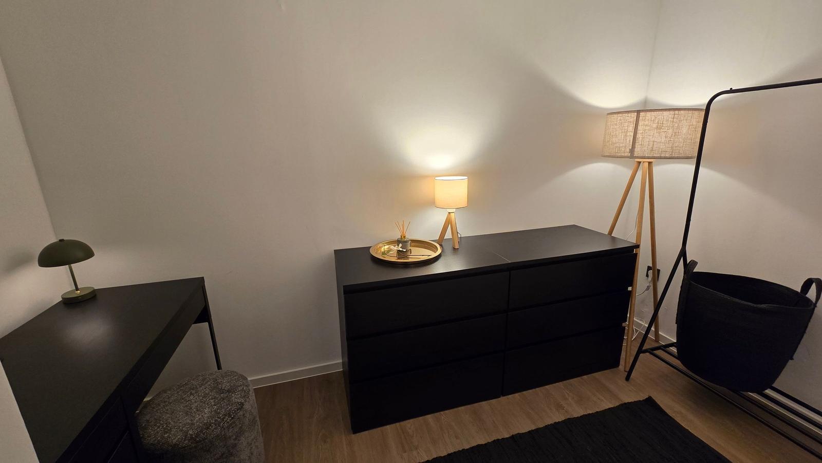 Schwarzer Schreibtisch mit Lampe, Schrank und Stehlampe in einem Raum mit Holzboden.