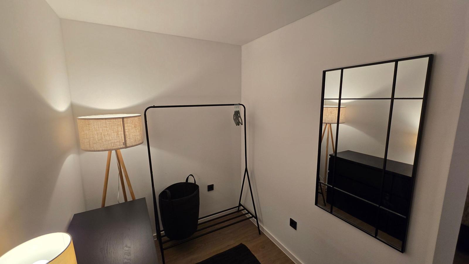 Schlafzimmer mit Kleiderständer, Spiegel und Stehlampe.