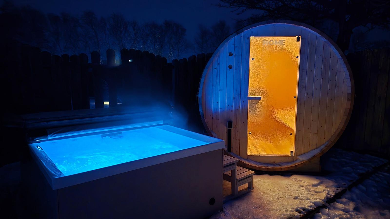 Ein beleuchteter Whirlpool und eine Holzsauna im Freien bei Nacht.