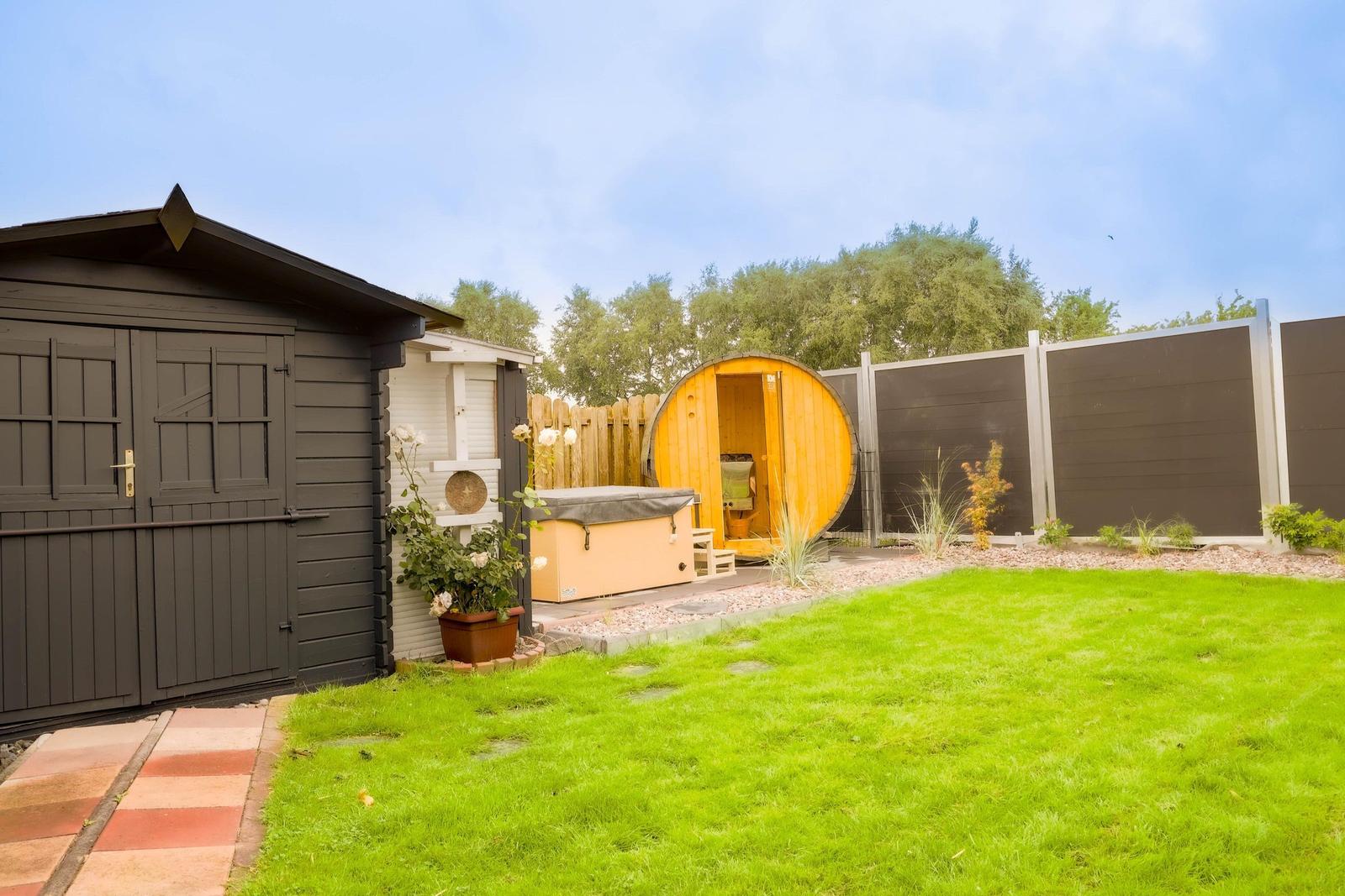 Hinterhof mit grünem Rasen, Holzgarage und runden Saunabaum.