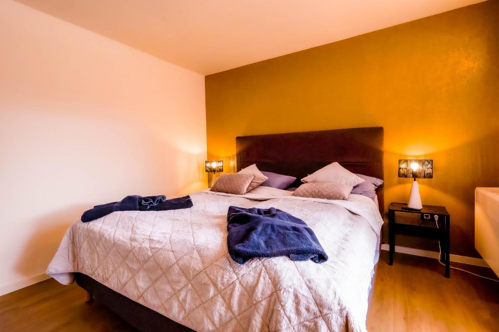 Schlafzimmer mit Bett, zwei Nachttischen und warm beleuchteten Wänden.