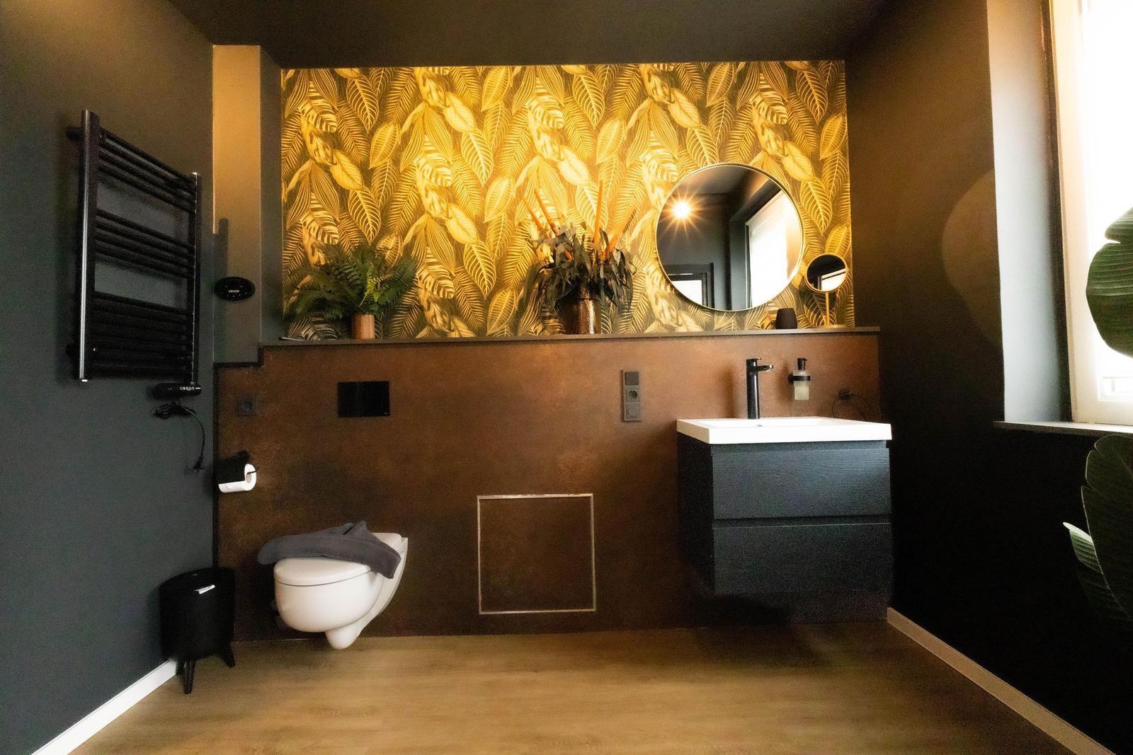 Bad mit goldfarbenem Blattmuster, Spiegel, Waschtisch und Toilette.