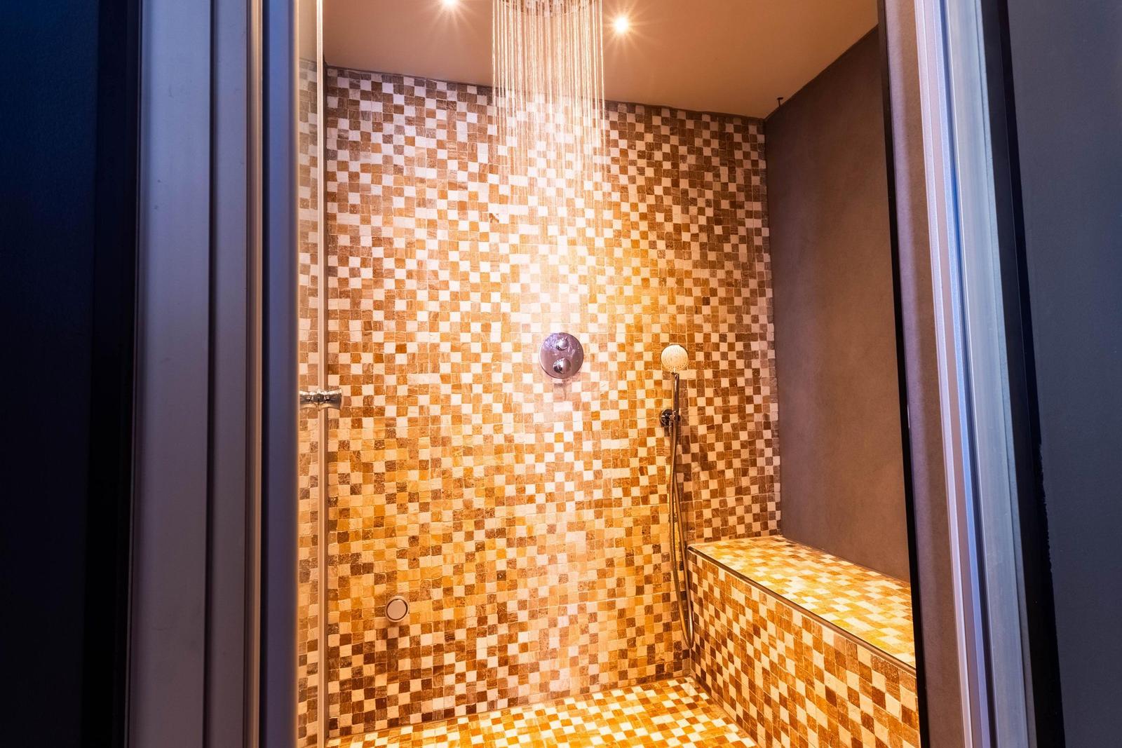 Dusche mit Mosaikfliesen, Regendusche und Sitzbank.