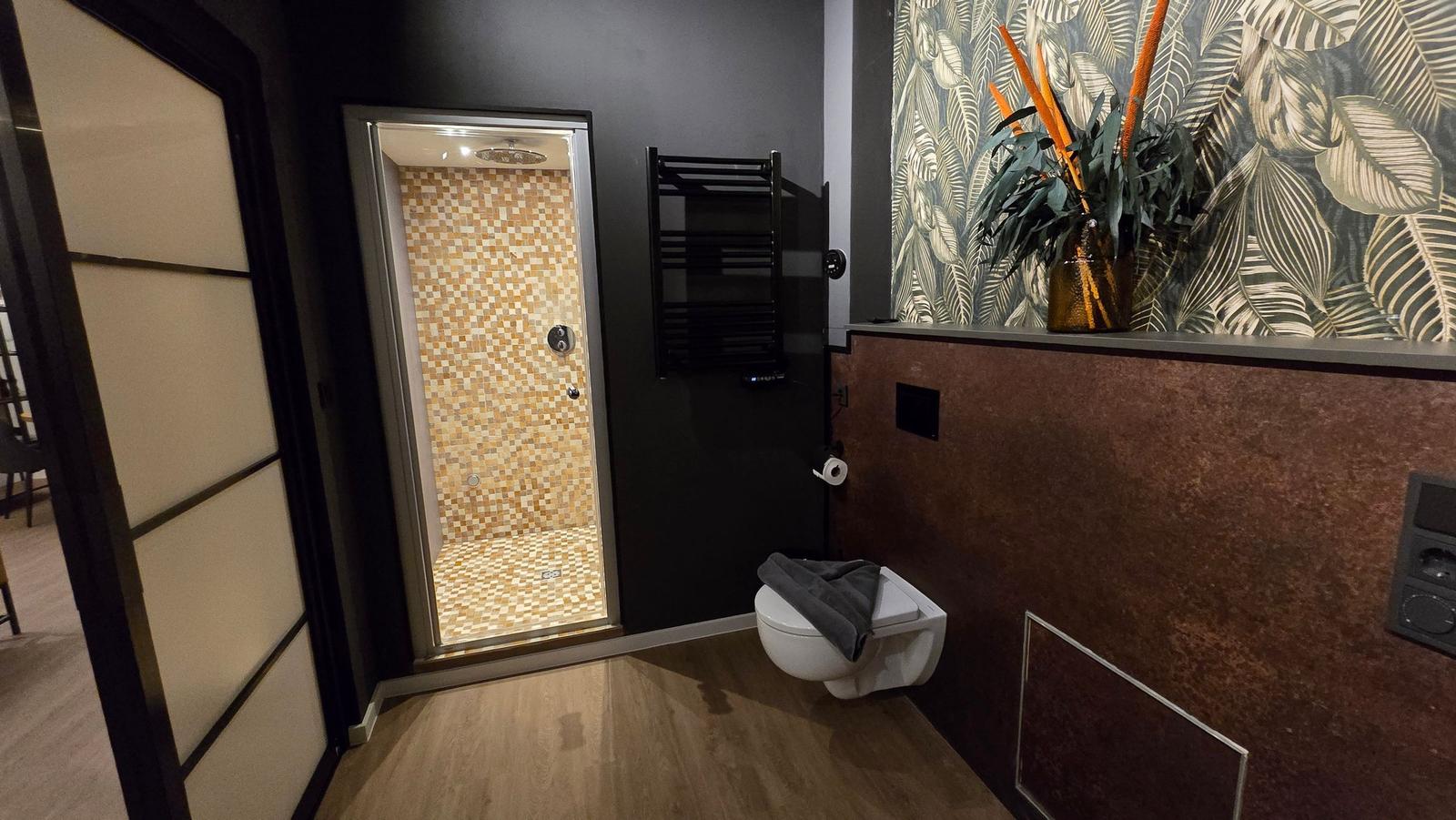 Bad mit Dusche, Toilette und Pflanze an der Wand.