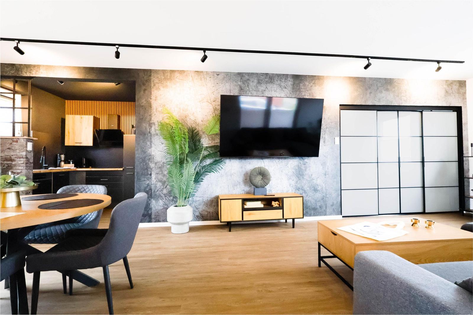 Wohn- und Essbereich mit TV, Pflanze und Küchenbereich im Hintergrund.