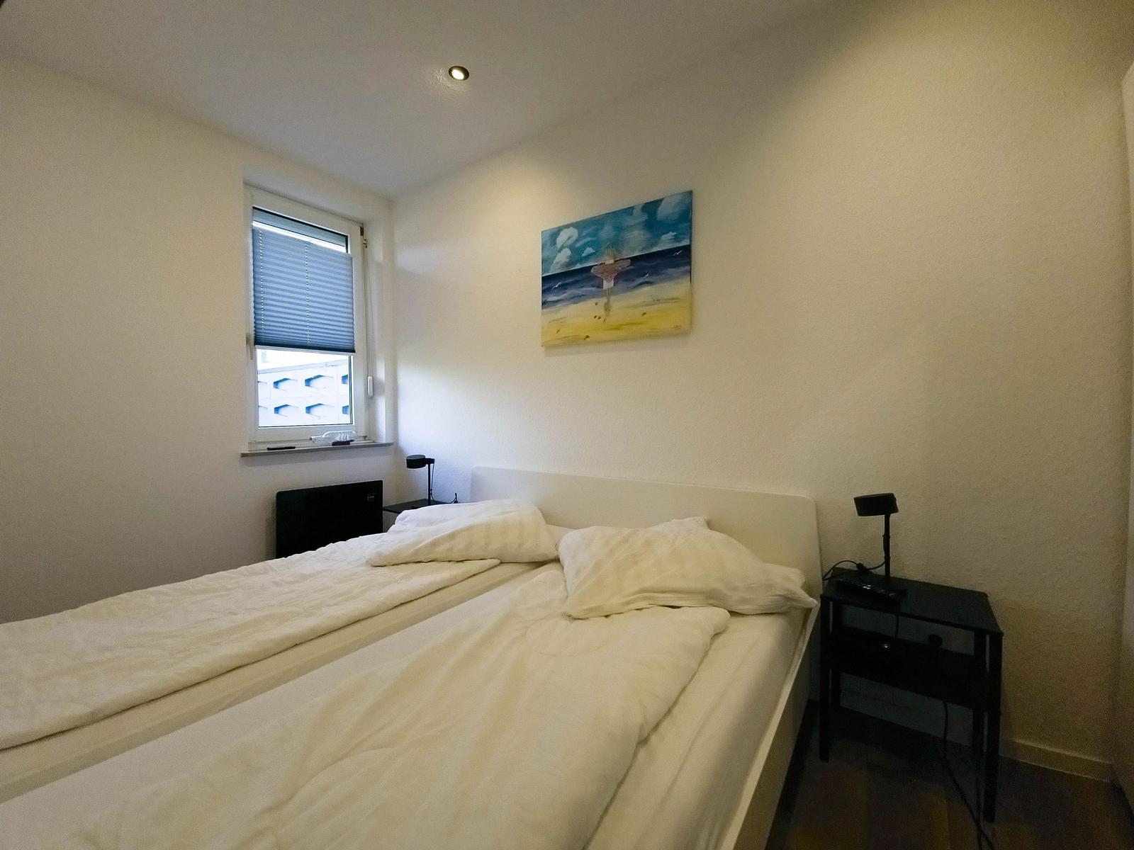 Bedroom with bed, nightstand, and wall art. Window with blinds.
