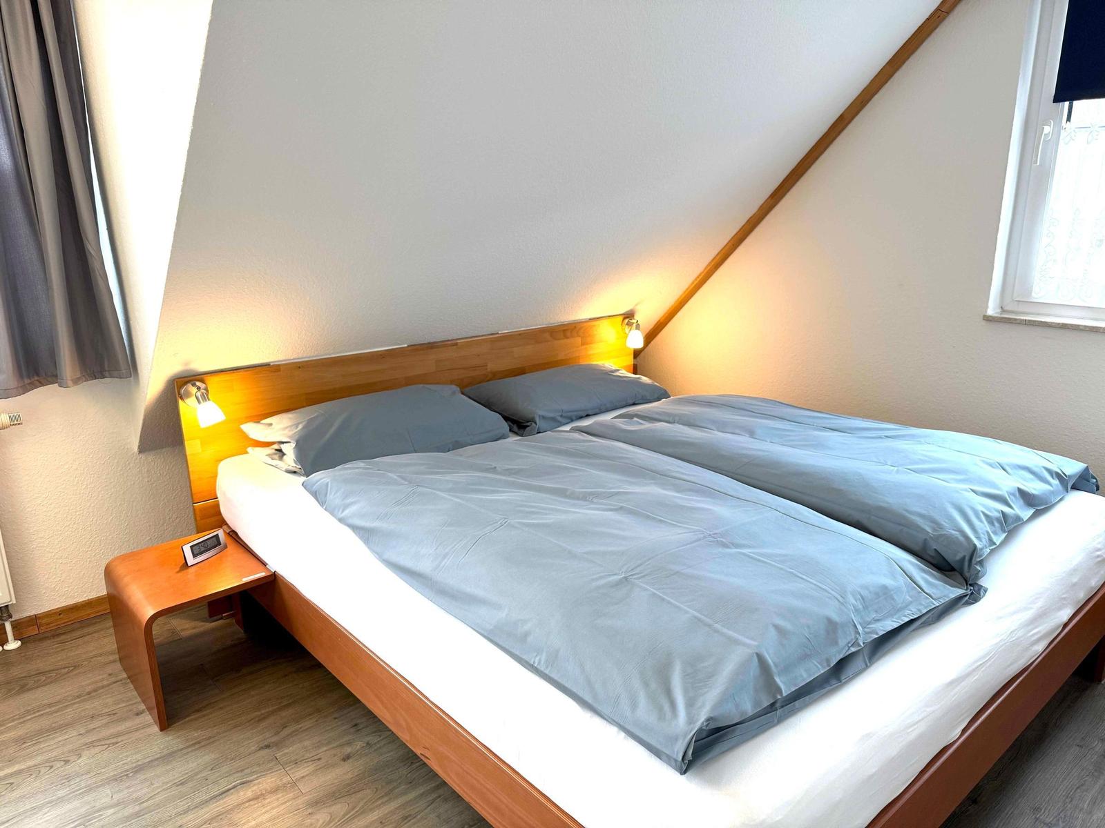 Ein Schlafzimmer mit Doppelbett, Holzrahmen und Fenster.