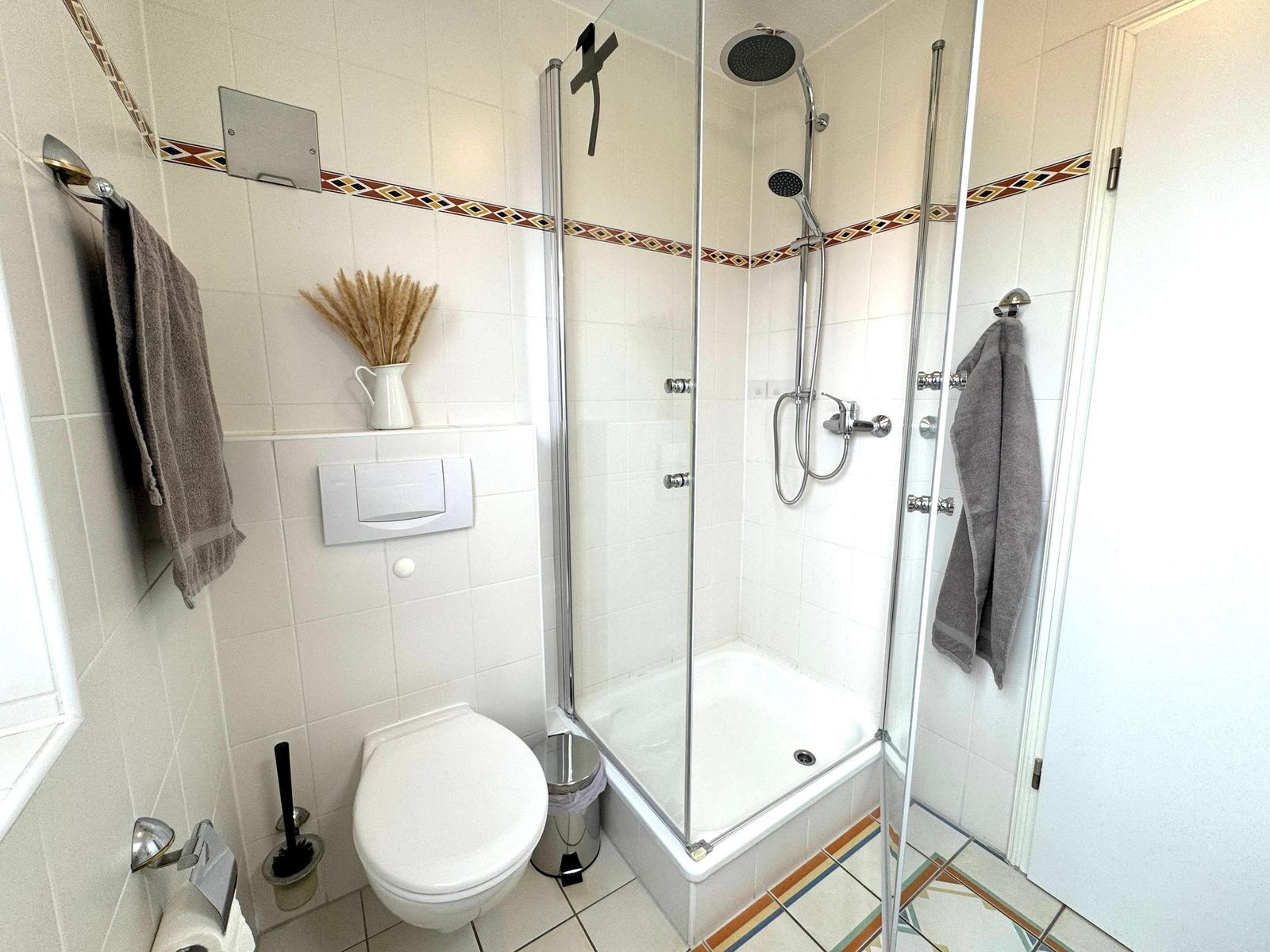 Badezimmer mit Dusche, Toilette und Handtuchhalter. Fliesen mit dekorativer Bordüre.