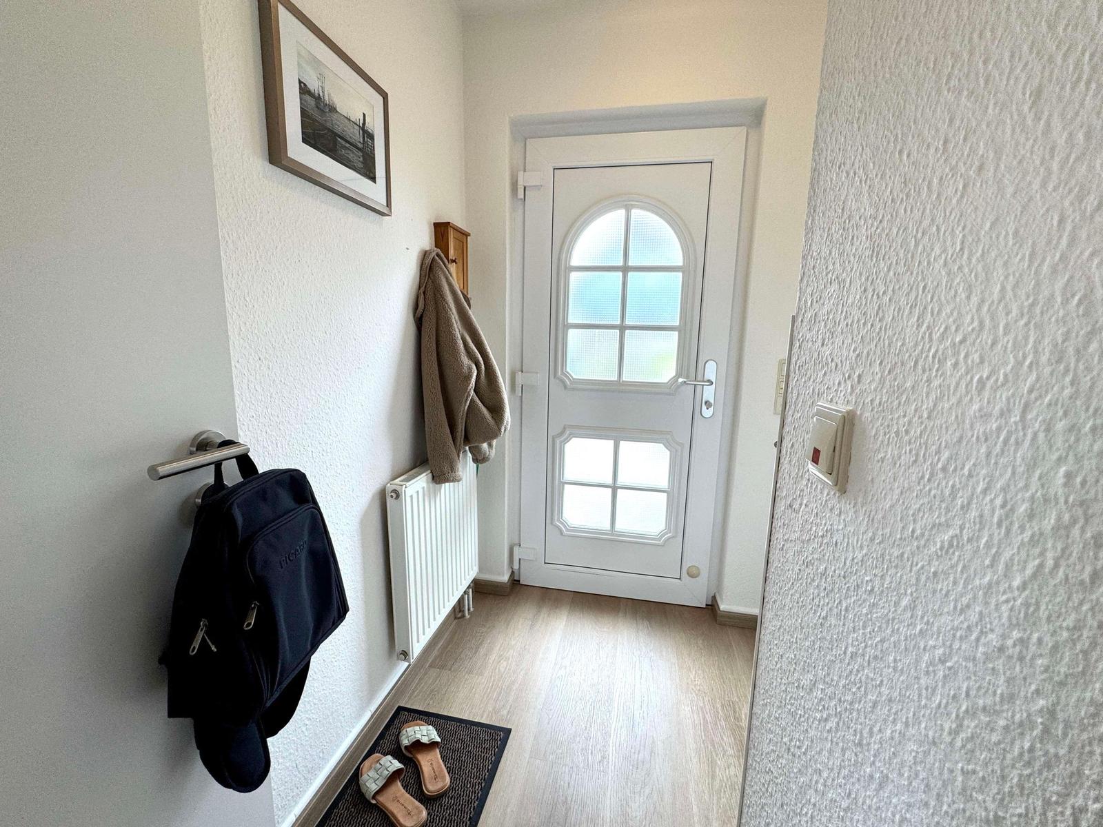 Eingangsbereich mit weiße Tür, Wandheizung und Wandhalterung für Rucksack.