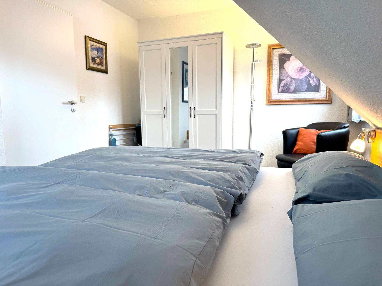 Schlafzimmer mit Doppelbett, Kleiderschrank und Sessel unter Dachschrägen.
