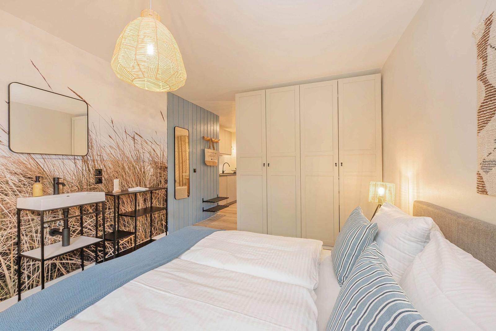 Schlafzimmer mit Bett, Kleiderschrank und Waschbecken mit Wandbild.