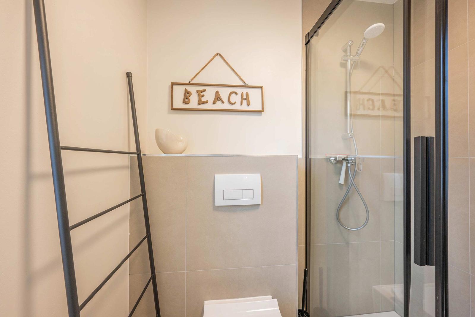 Badezimmer mit Dusche, Toilette und Wanddekoration mit BEACH.