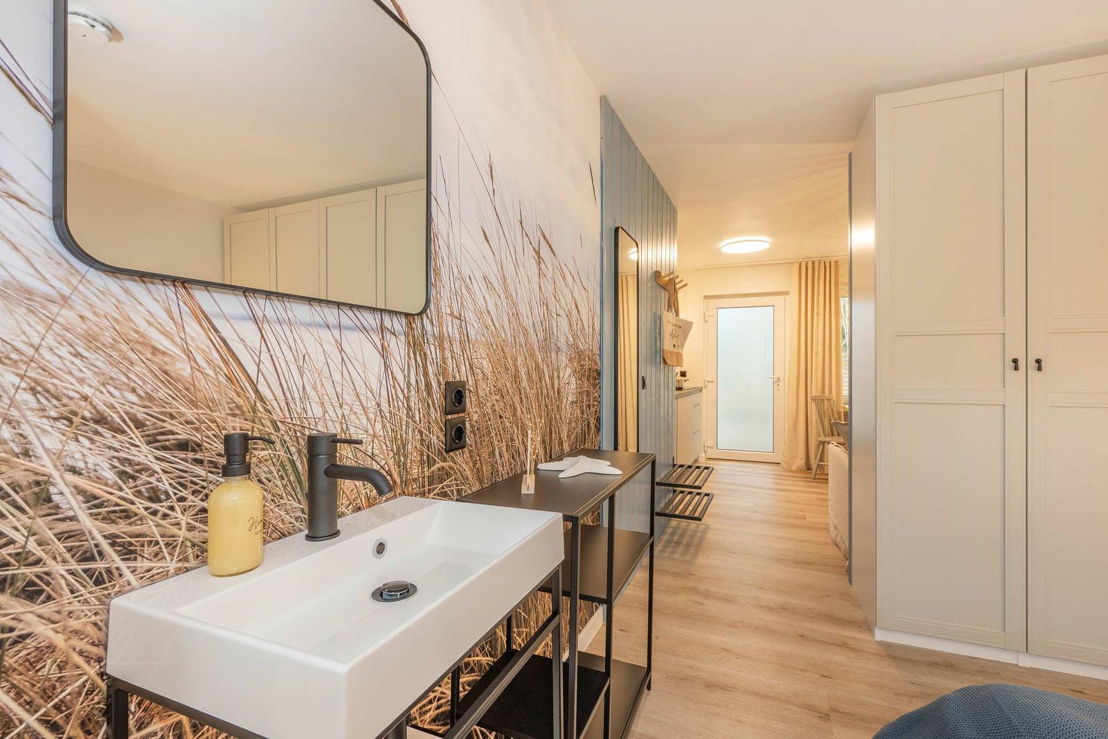 Bad mit Waschbecken, Spiegel und Pflanzenwand. Flur mit Kleiderschrank und Tür.