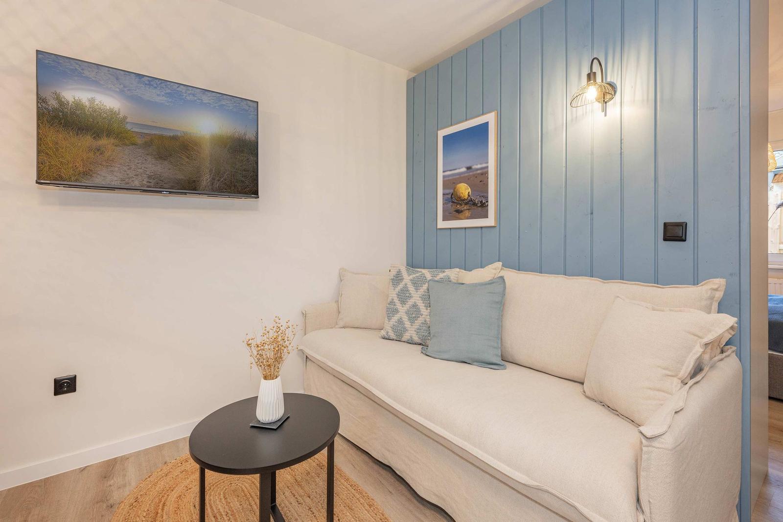 Ein Wohnbereich mit Sofa, kleinem Tisch und Wandbildern. Eine blaue Holzwand und eine Wandtafel.