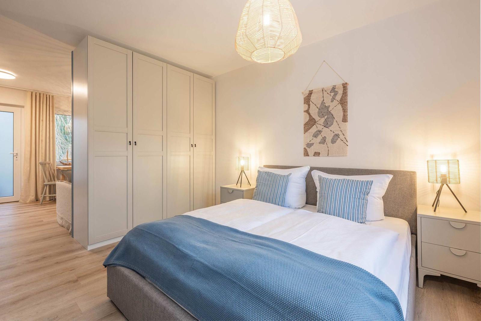 Schlafzimmer mit Bett, Kleiderschrank und Nachttischen. Deckenleuchte und Wanddekoration.
