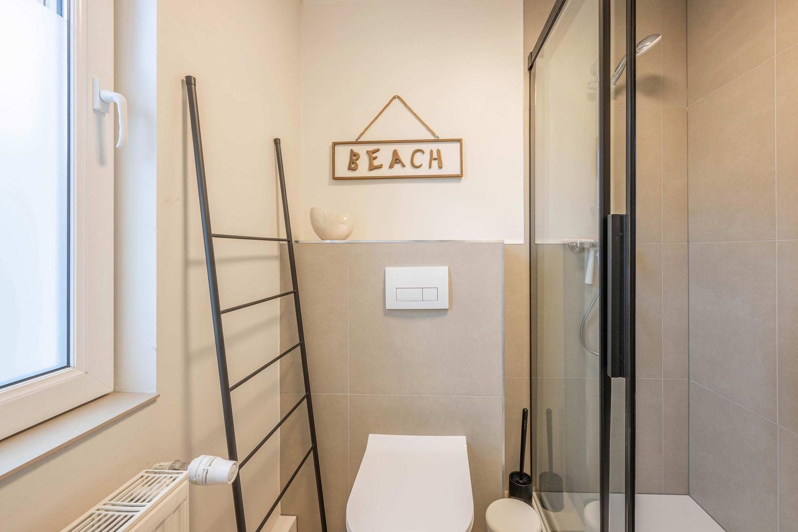 Bad mit Dusche, Toilette und Fenster. Wanddekoration mit BEACH.