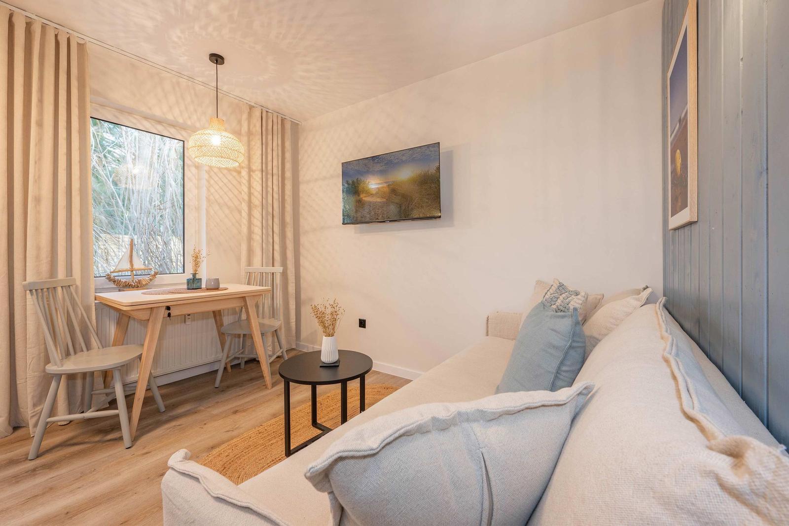 Wohnzimmer mit Sofa, Esstisch und Fernseher an der Wand.