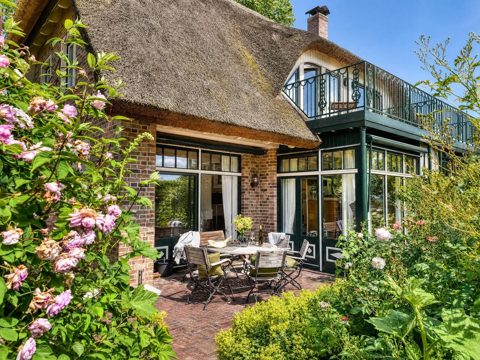 Haus mit Strohdach, Terrasse und Garten mit Blumen.