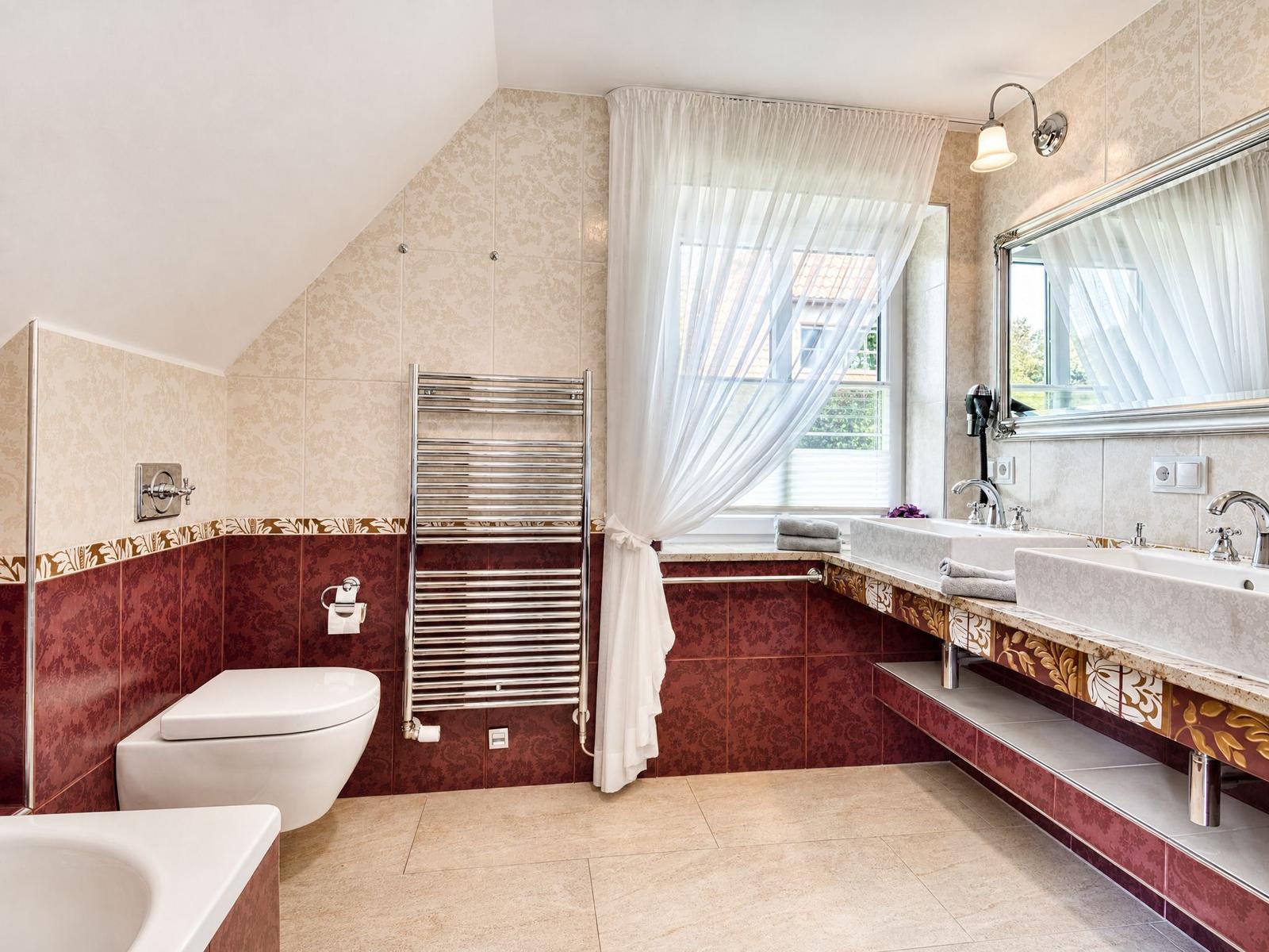 Badezimmer mit Dusche, Waschbecken und Toilette. Fenster mit Vorhang. Wandverkleidung in Rot und Beige.