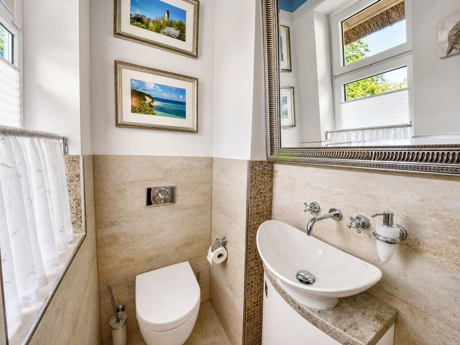 Badezimmer mit Toilette, Waschbecken und Spiegel. Wandverkleidung aus Stein. Fenster mit Blick nach draußen.