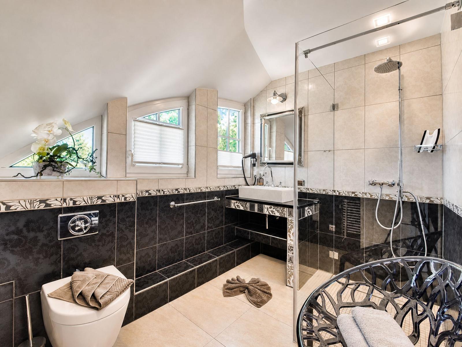 Badezimmer mit Dusche, Waschbecken und Toilette. Fenster und dekorative Fliesen.